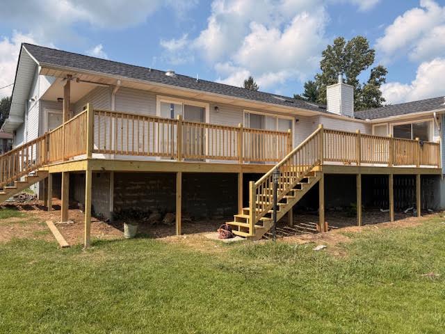 Full-width pressure-treated deck spanning the back of a white ranch home with railing and stairs