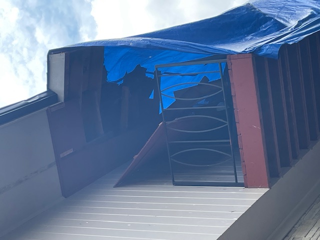 Before: storm-damaged porch roof overhang covered with a blue tarp